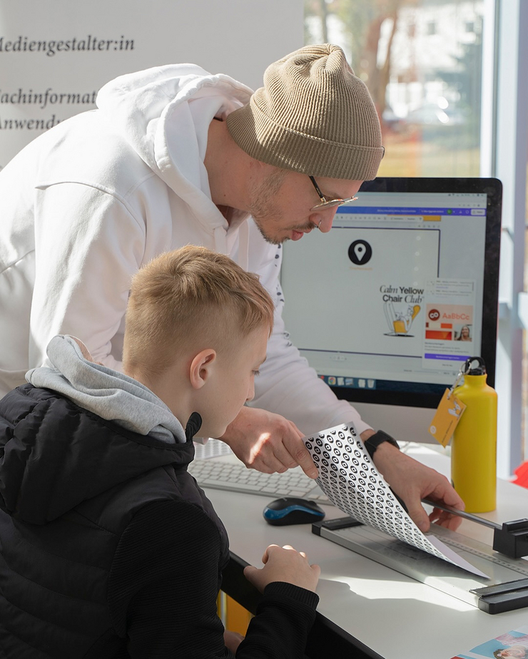 C3 auf der Ausbildungsmesse Weiden 2025 Ein Mitarbeiter der C3 Werbeagentur zeigt einem Jungen, wie man ein selbst gestaltetes Namensschild zuschneidet